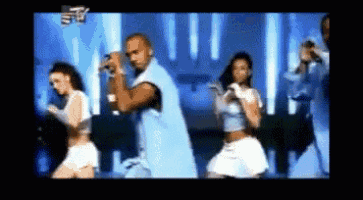 a man is singing into a microphone while two women dance in front of him on a tv screen