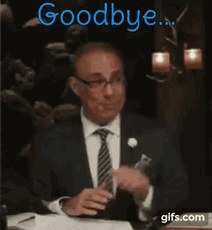 a man in a suit and tie is sitting at a table and says goodbye