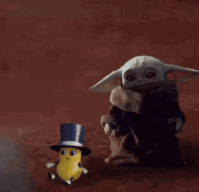 a baby yoda from star wars is holding a tennis ball in his mouth .