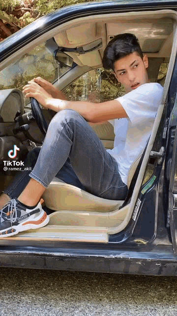 a young man is sitting in the driver 's seat of a car with a tiktok watermark