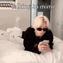 a person wearing sunglasses is laying on a bed talking to mimi .