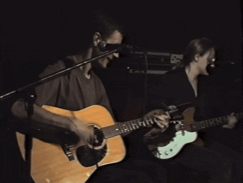 a man singing into a microphone while a woman plays guitar