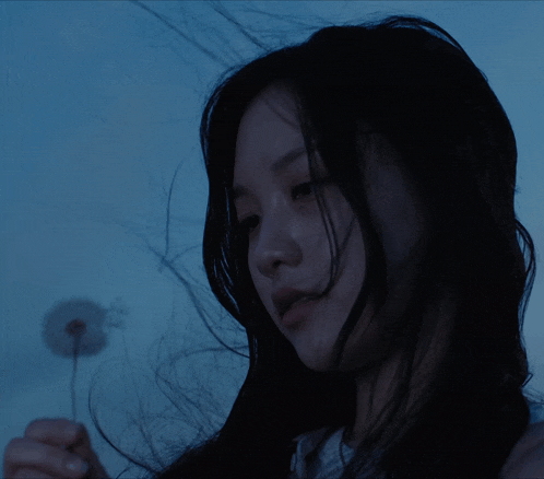 a woman holding a dandelion in her hand in the dark