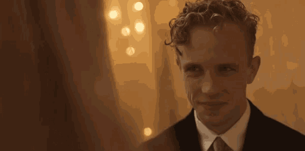 a man with curly hair wearing a suit and tie is smiling