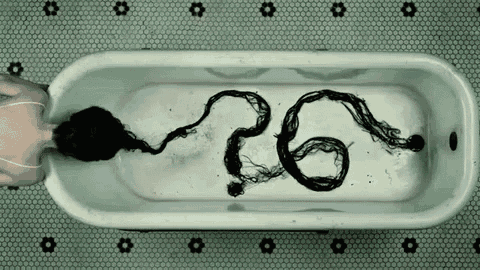 a woman is laying in a bathtub with her hair coming out of it and the number 26 on the floor .