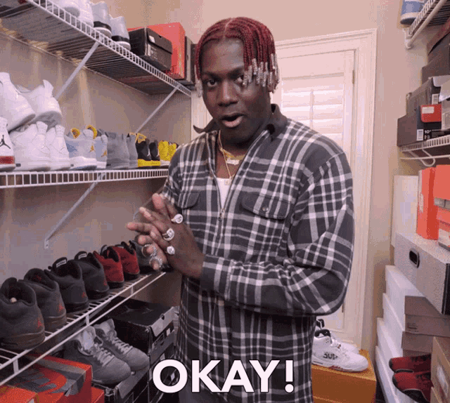 a man in a plaid shirt is standing in front of a shelf full of shoes and says okay