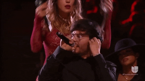 a man is holding a microphone in front of his ear while a woman stands behind him