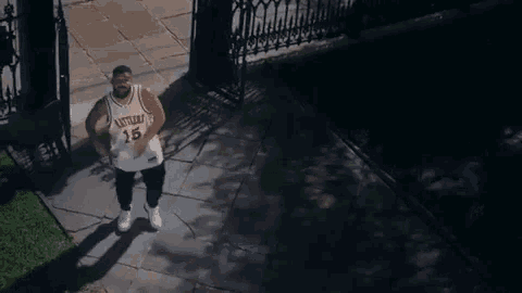 a man wearing a basketball jersey with the number 15 on it is standing on a sidewalk .