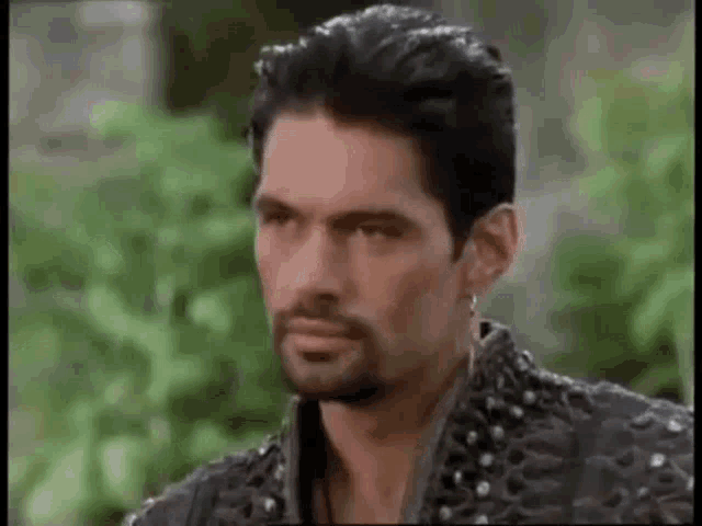 a man with a beard is wearing a black jacket with studs and earrings .