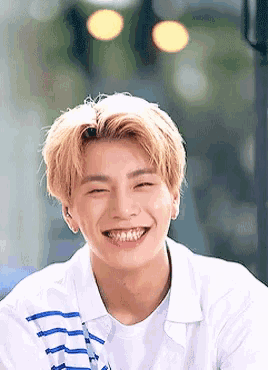 a young man with blonde hair is smiling for the camera while wearing a white shirt .