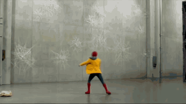 a person in a yellow jacket is jumping in front of a wall with snowflakes painted on it