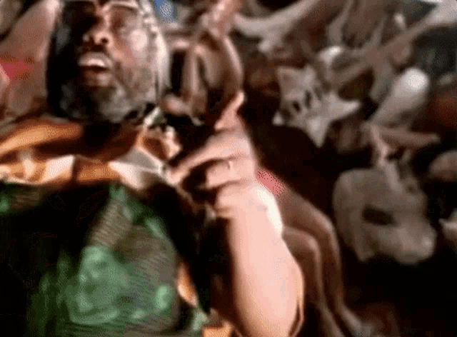 a man with a beard and glasses is standing in front of a pile of bones .