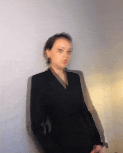 a blurry photo of a woman in a black suit leaning against a wall