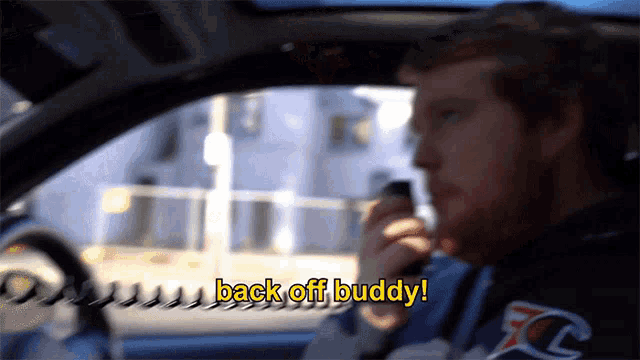 a man sitting in a car talking on a cell phone with the words back off buddy above him