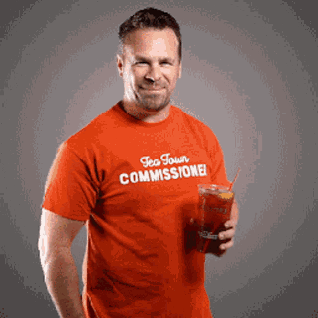 a man wearing an orange tea town commissioner t-shirt holds a drink
