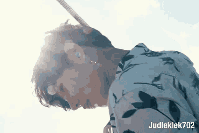 a man in a floral shirt is looking up at the sky with judleklek702 written below him
