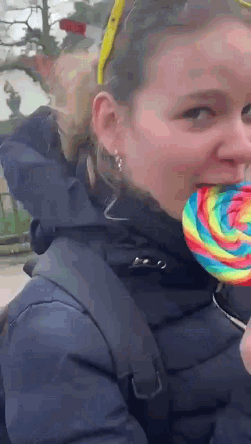 a woman is eating a rainbow colored lollipop while wearing a black jacket