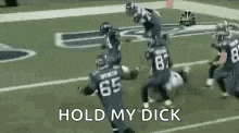 a group of football players are running on a field with the words `` hold my dick '' in the background .