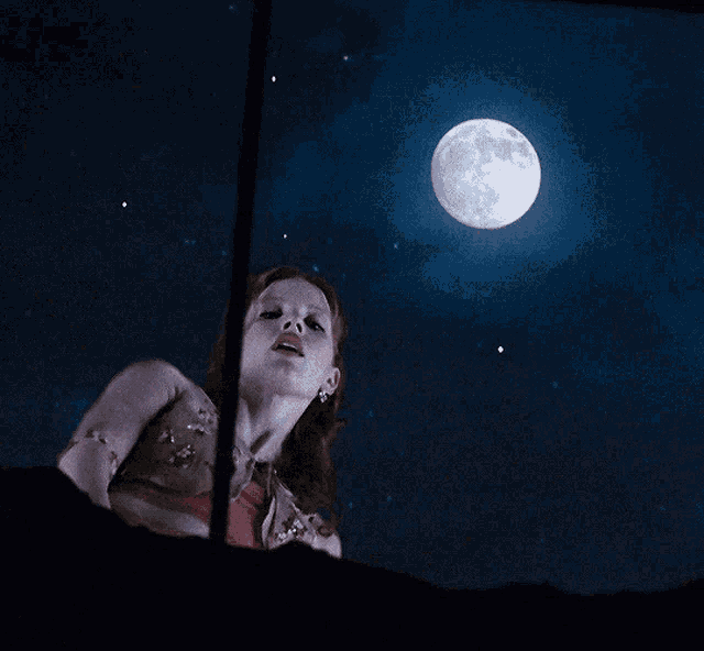 a woman stands in front of a full moon in a dark sky