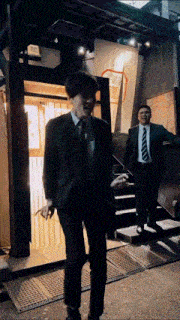 a man in a suit and tie is smoking a cigarette in front of a building