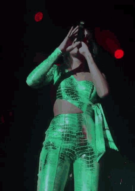 a woman in a green outfit is singing into a microphone on stage