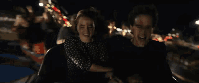 a man and a woman are riding a roller coaster at an amusement park at night .
