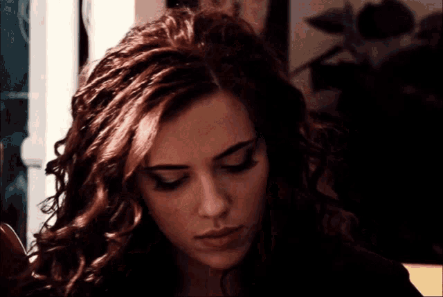 a woman with curly red hair looks down at something