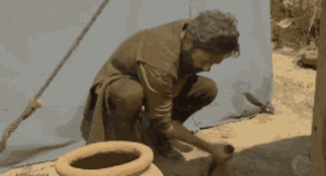 a man kneeling down next to a large pot