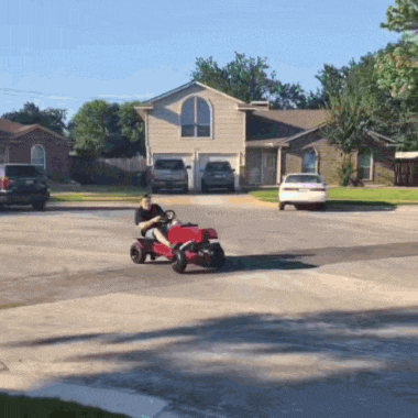 a man riding a red lawn mower down a street