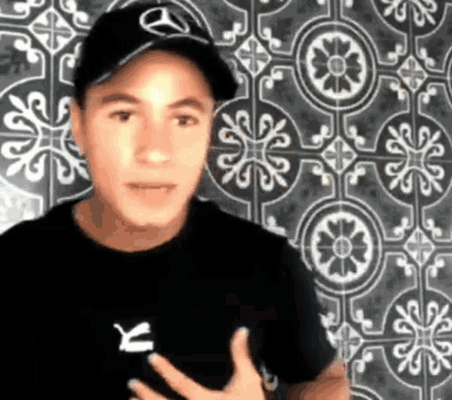 a young man wearing a hat and a black shirt is standing in front of a tiled wall .