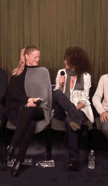 a woman with a microphone sits next to another woman with a ponytail