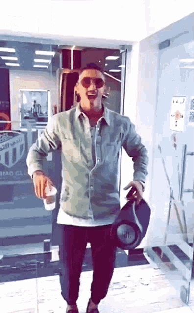 a man wearing sunglasses is holding a jbl speaker and a cup