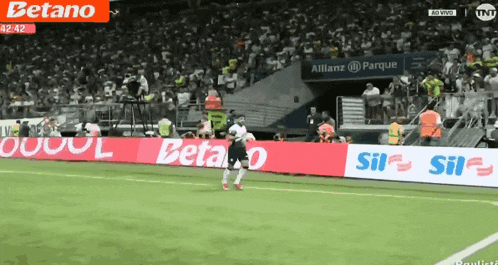 a soccer player runs across a field with advertisements for betano and sil
