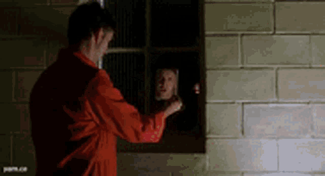 a man in an orange uniform looks out a window at another man