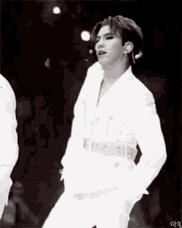 a black and white photo of a man in a white suit dancing on stage .