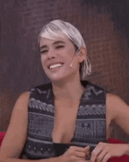 a woman in a plunging neckline vest is sitting on a couch and making a face .
