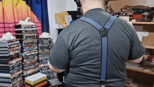 a man wearing suspenders stands in front of a stack of dvds and a sign that says " i love you "