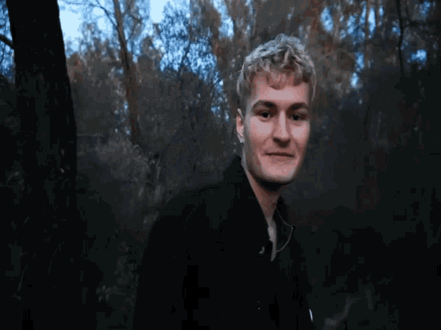 a man in a black jacket stands in the woods