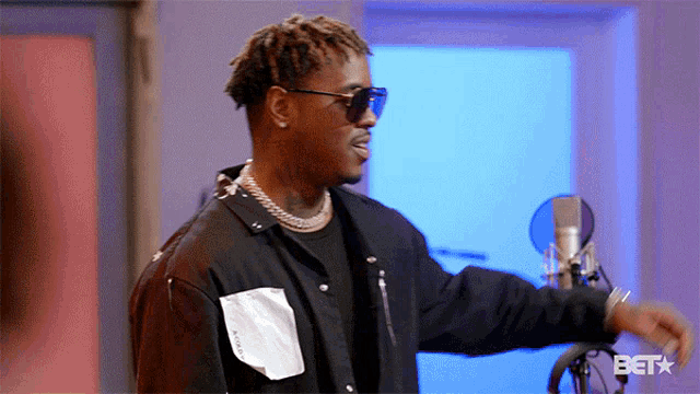 a man wearing sunglasses is standing in front of a microphone with the bet logo in the corner