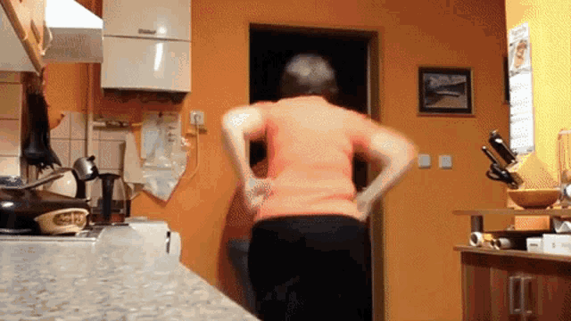 a woman in an orange shirt is standing in a kitchen next to a wall with a calendar on it