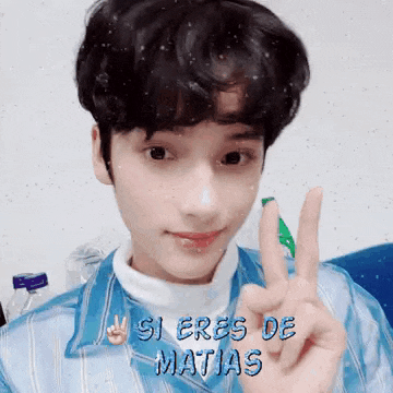 a young man in a blue shirt is giving a peace sign
