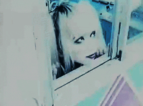 a woman with white hair and black eyes is looking out a window