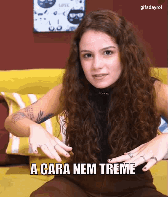 a woman with curly hair is sitting on a yellow couch with the words a cara nem treme below her