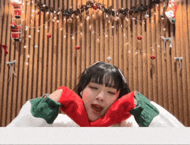 a girl making a heart with her hands in front of a wall with christmas lights