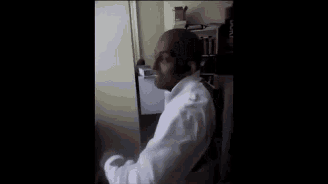 a man in a white sweater is sitting in a chair in a dark room .