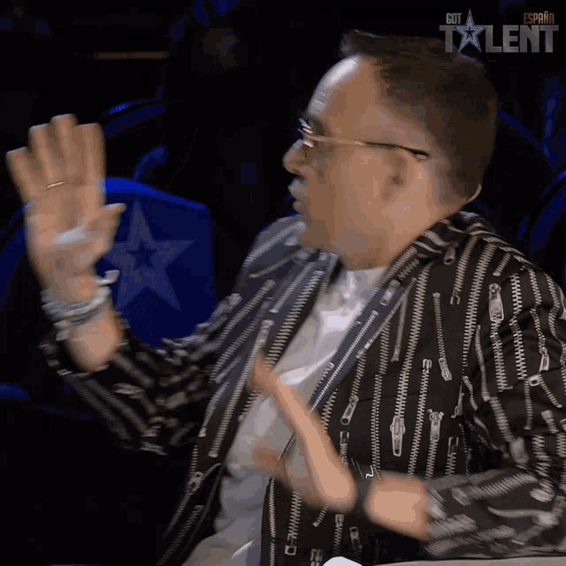 a man wearing a black and white jacket with zippers on it is sitting in front of a sign that says got talent