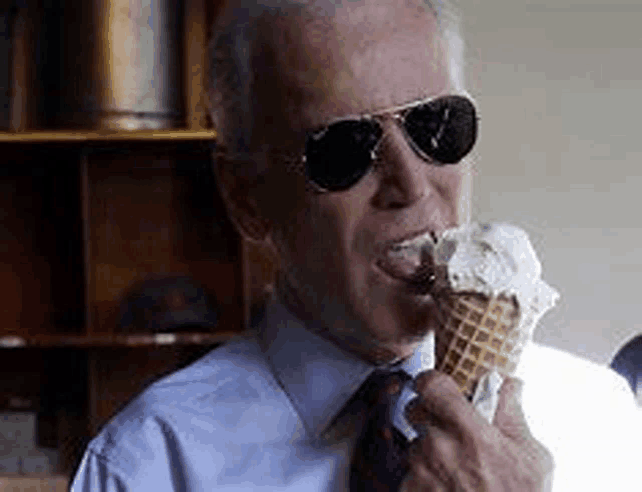 a man in a suit and tie is eating an ice cream cone while wearing sunglasses .