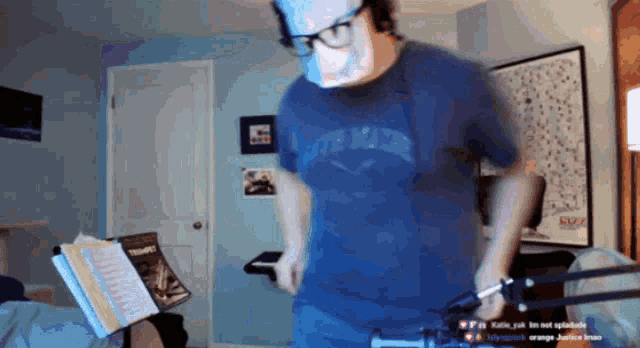 a man wearing a blue shirt that says justice league is standing in a room