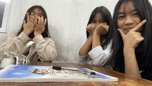 three girls are sitting at a table with a book on it that says ' a ' on it