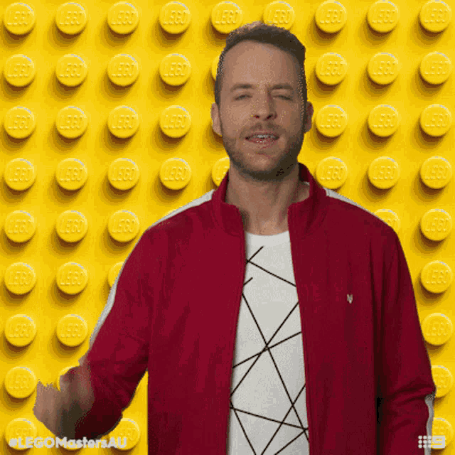 a man in a red jacket stands in front of a lego wall